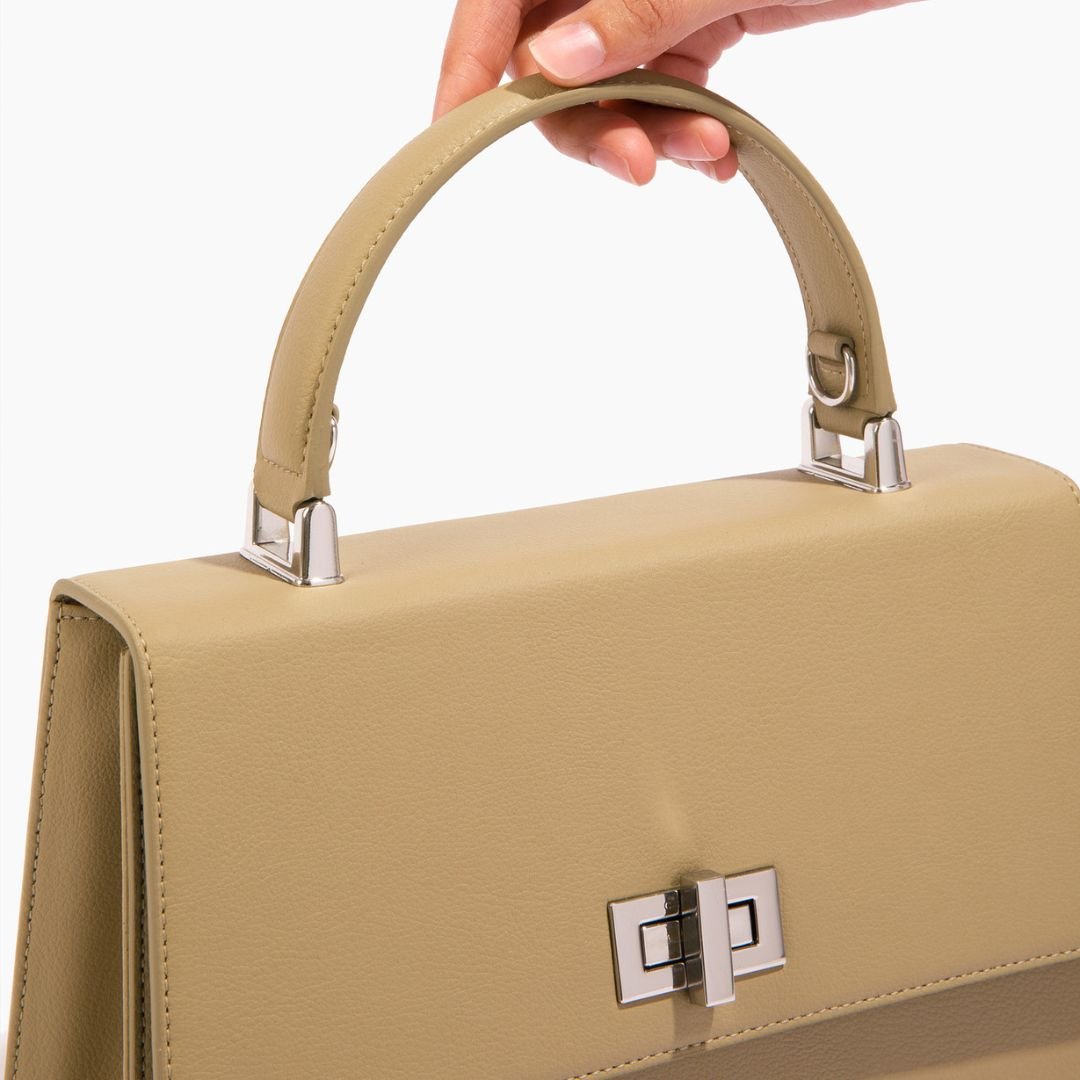 A detailed shot of the handle attachment on the beige She-EO handbag, showing silver hardware and precise stitching