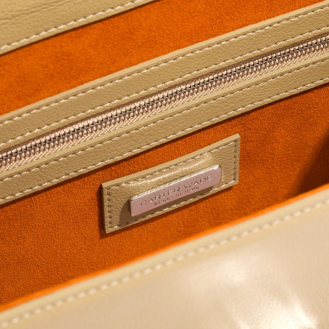 A close-up view of the interior of the beige She-EO handbag, featuring a rich burnt-orange vegan suede lining and a zippered pocket