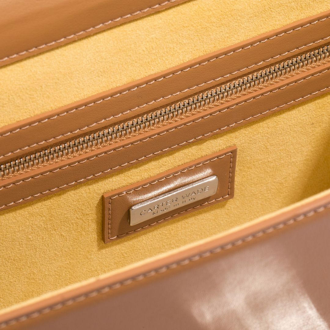 Interior view of a Carter Wade handbag in brown grape leather, featuring a luxurious yellow suede lining and a silver engraved brand plaque