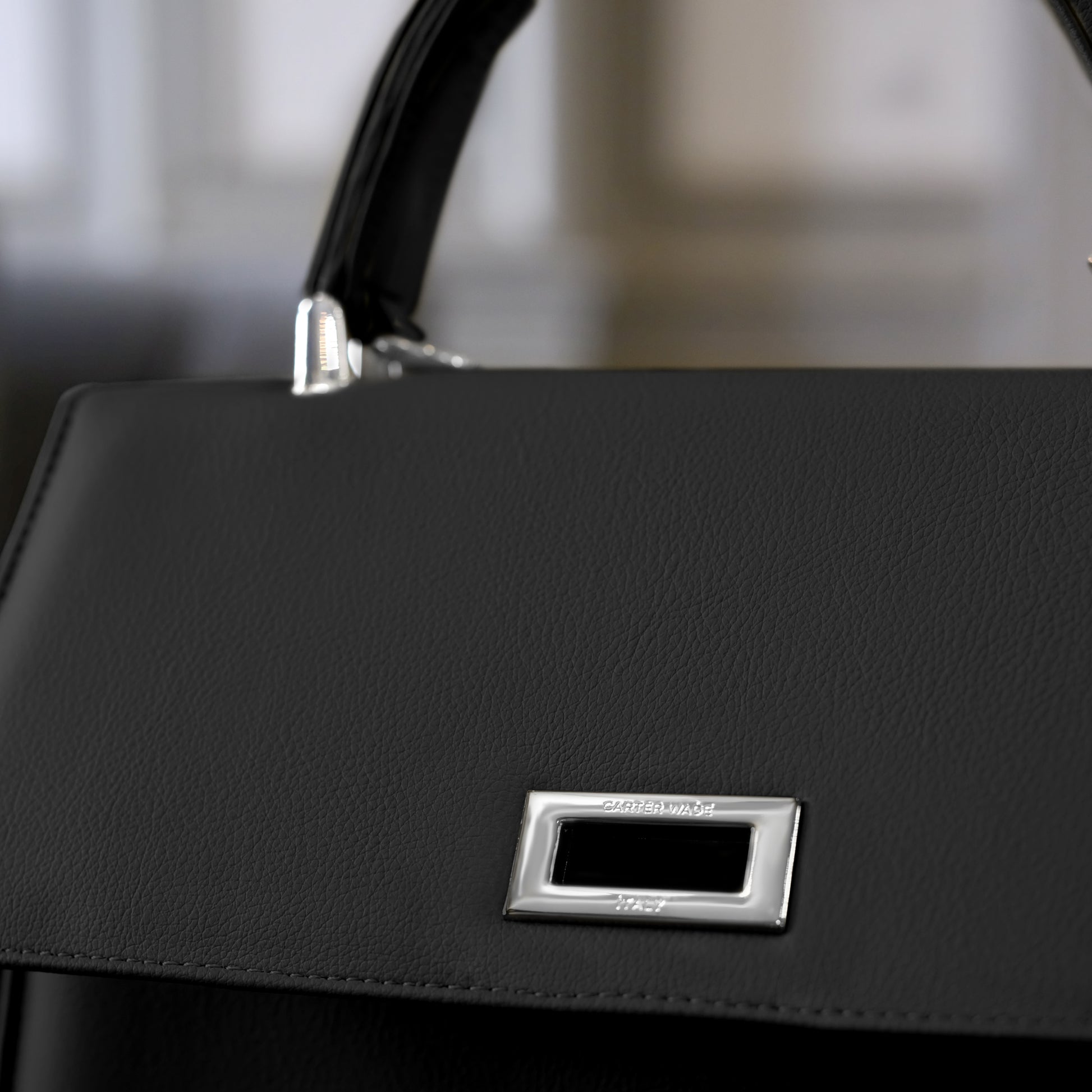 A close-up of the Carter Wade silver logo hardware on a black cactus handmade handbag, highlighting luxurious detailing