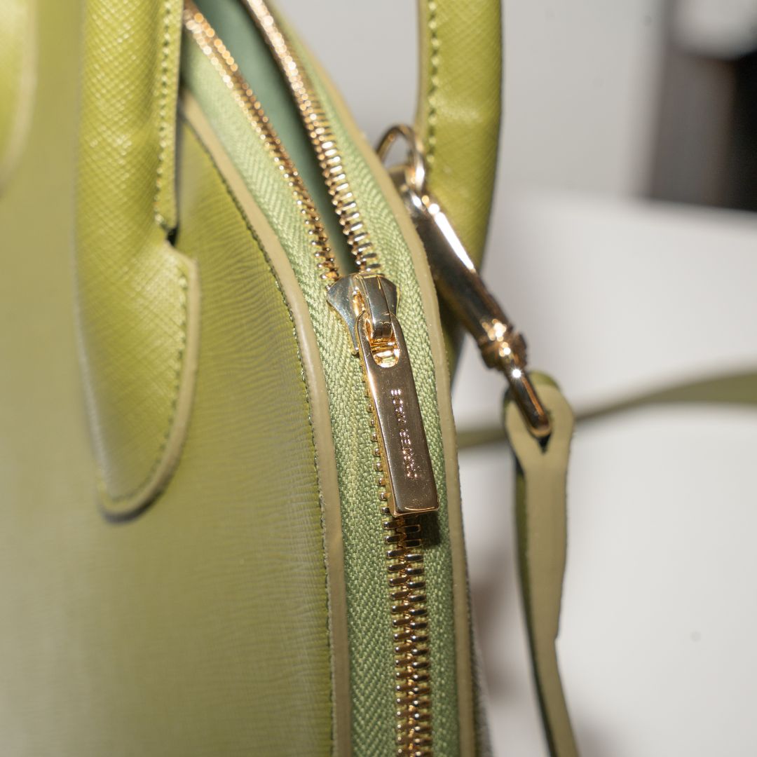 A macro shot of Ms. Lady Luck in Olive Green, highlighting the engraved Carter Wade gold zipper and fine stitching on the vegan cactus leather exterior.