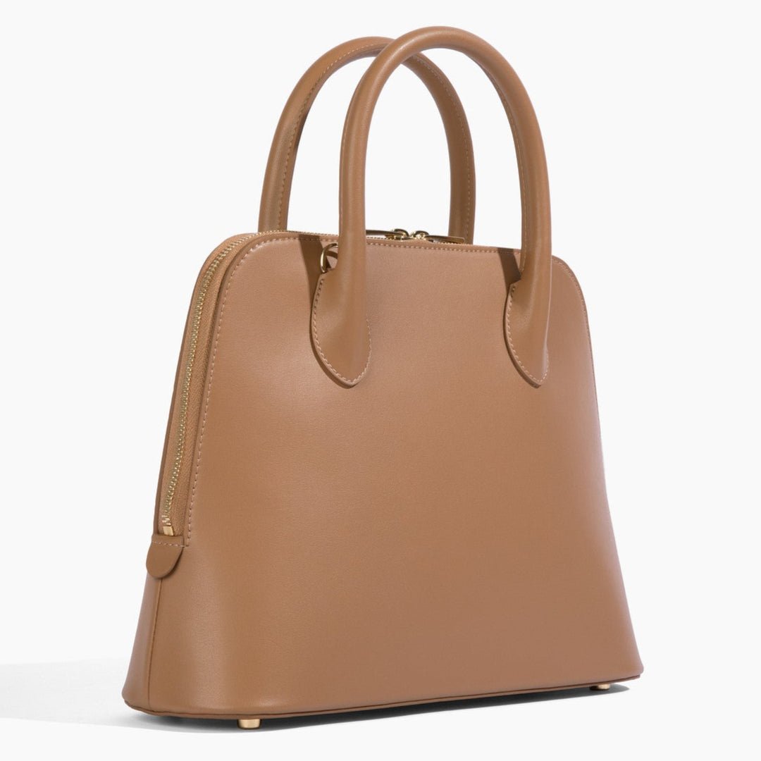 A side-angled view of the Ms. Lady Luck handbag in brown vegan grape leather, showcasing its structured silhouette, smooth finish, and elegant gold hardware