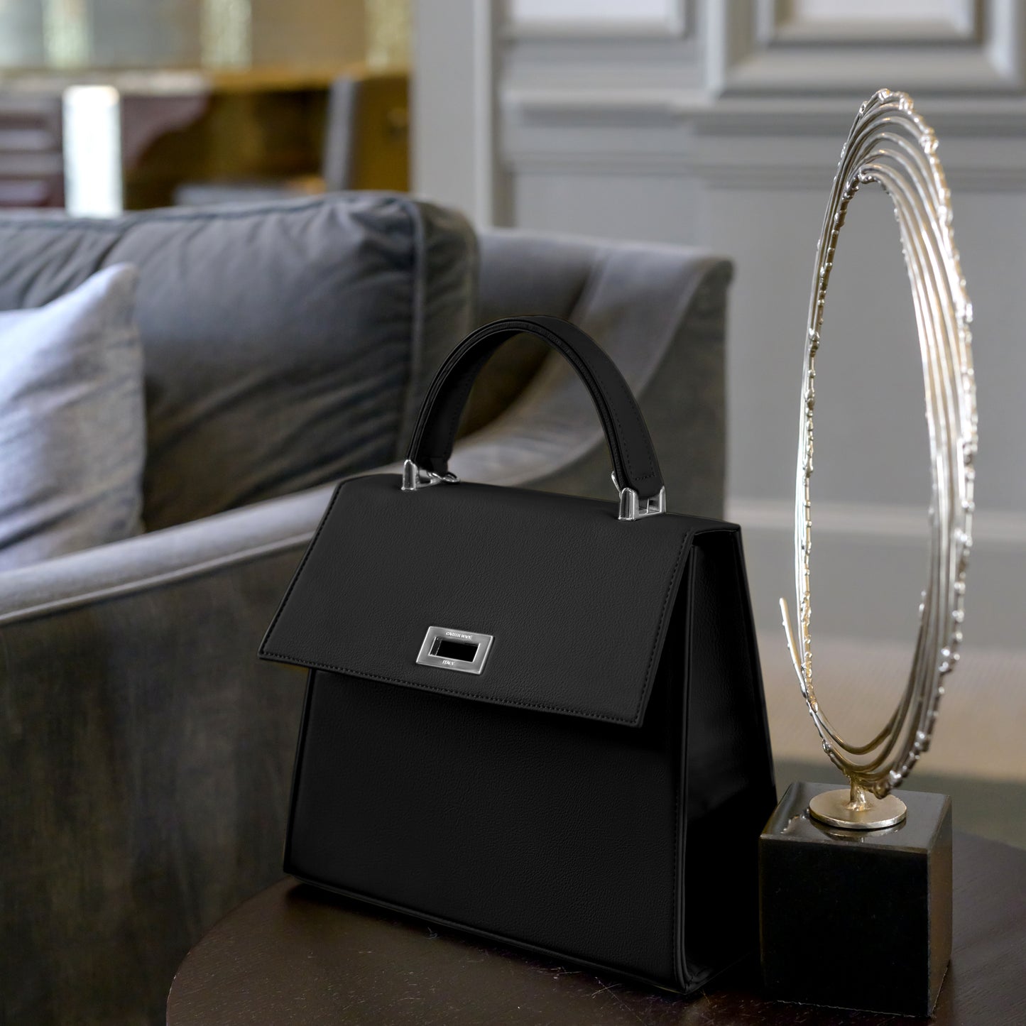 Side view of a structured black Carter Wade handbag made with cactus leather with a silver turn-lock closure and top handle, exuding timeless elegance sitting on chic end table
