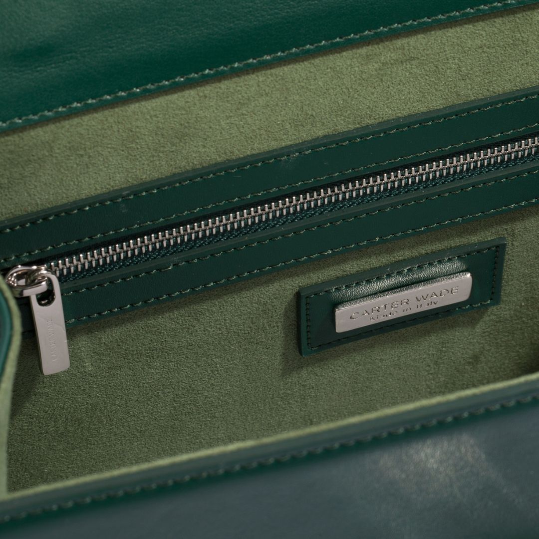 Interior view of a dark green handbag featuring high-quality vegan suede lining and elegant silver hardware on the zipper, designed by Carter Wade.