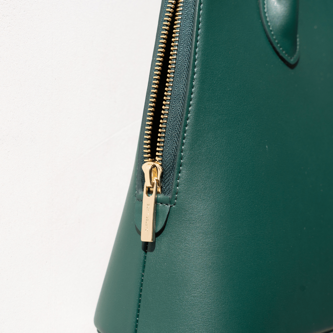A macro shot of the handbag’s gold zipper and side panel, showcasing the engraved hardware and fine detailing. The sturdy stitching and refined craftsmanship reflect the brand’s dedication to quality.