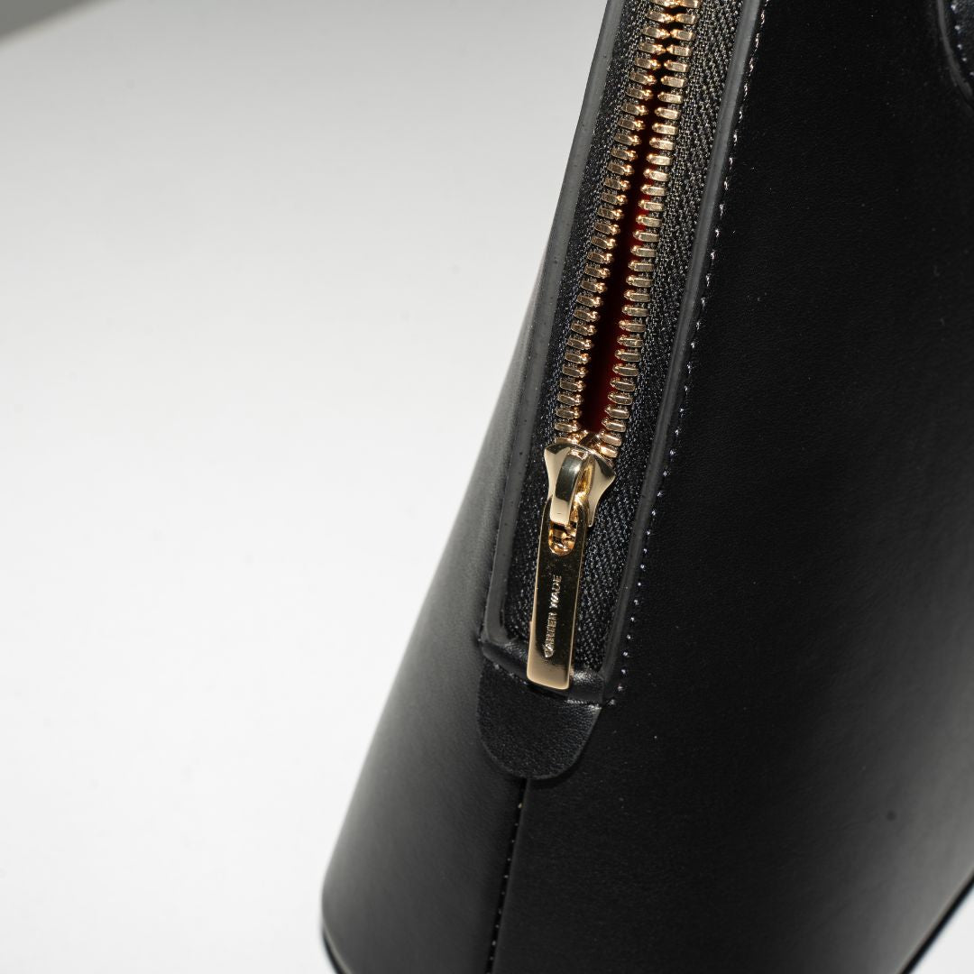 A macro shot of the Ms. Lady Luck handbag’s gold zipper and structured leather finish. The high-quality vegan leather is complemented by precision stitching and polished gold hardware for a sophisticated look.