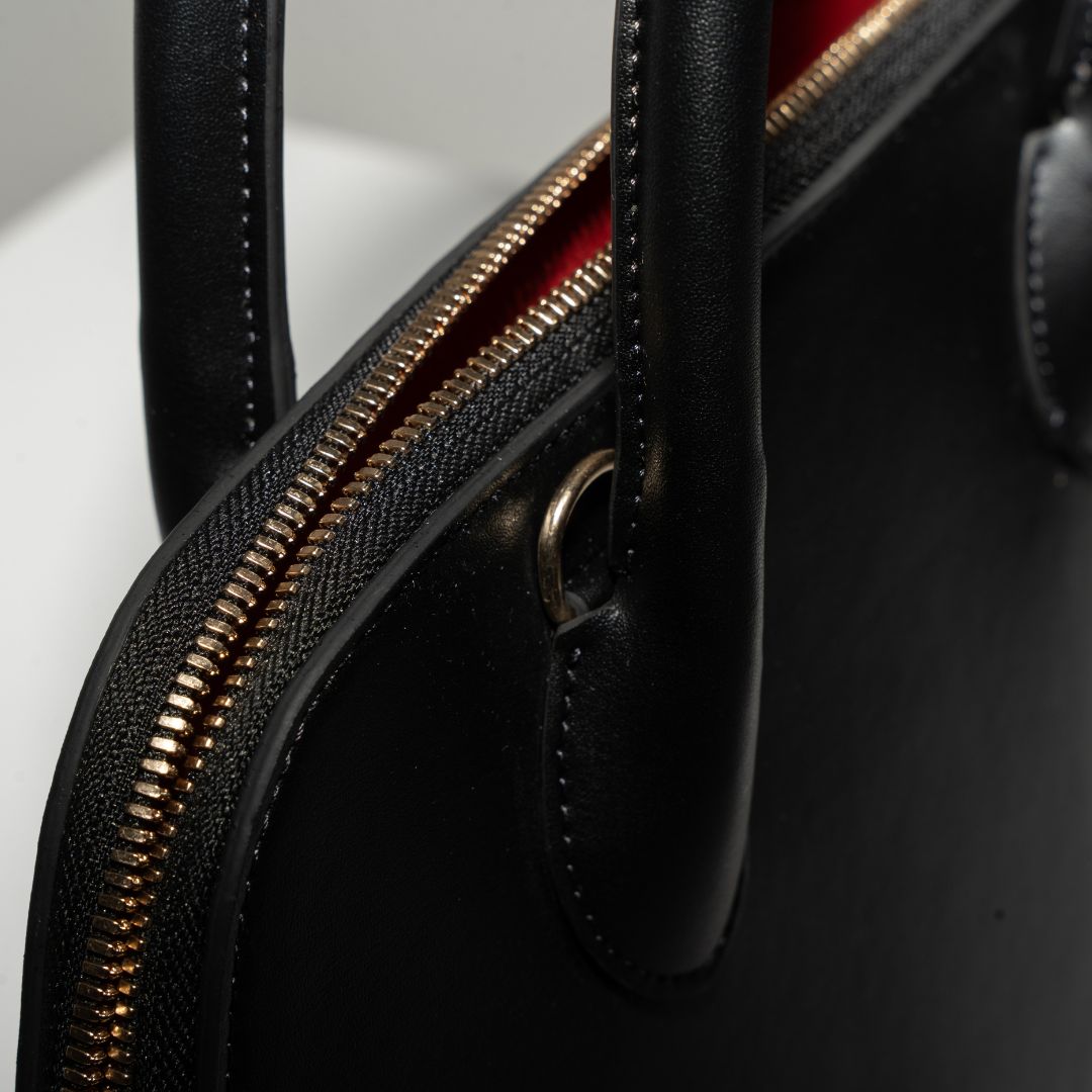 A detailed view of the handbag’s sturdy top handles and gold zipper closure. The reinforced handles and smooth grape leather ensure durability, while the soft red interior lining peeks through the zipper for a luxurious contrast.