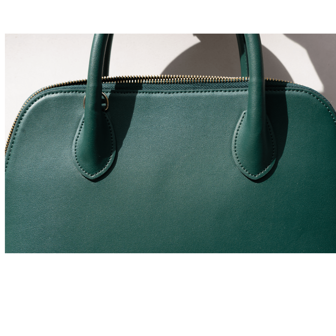 A detailed close-up of the bag’s front, capturing the smooth texture of the green vegan leather under natural sunlight. The soft shadows highlight the elegant structure and minimalist design.