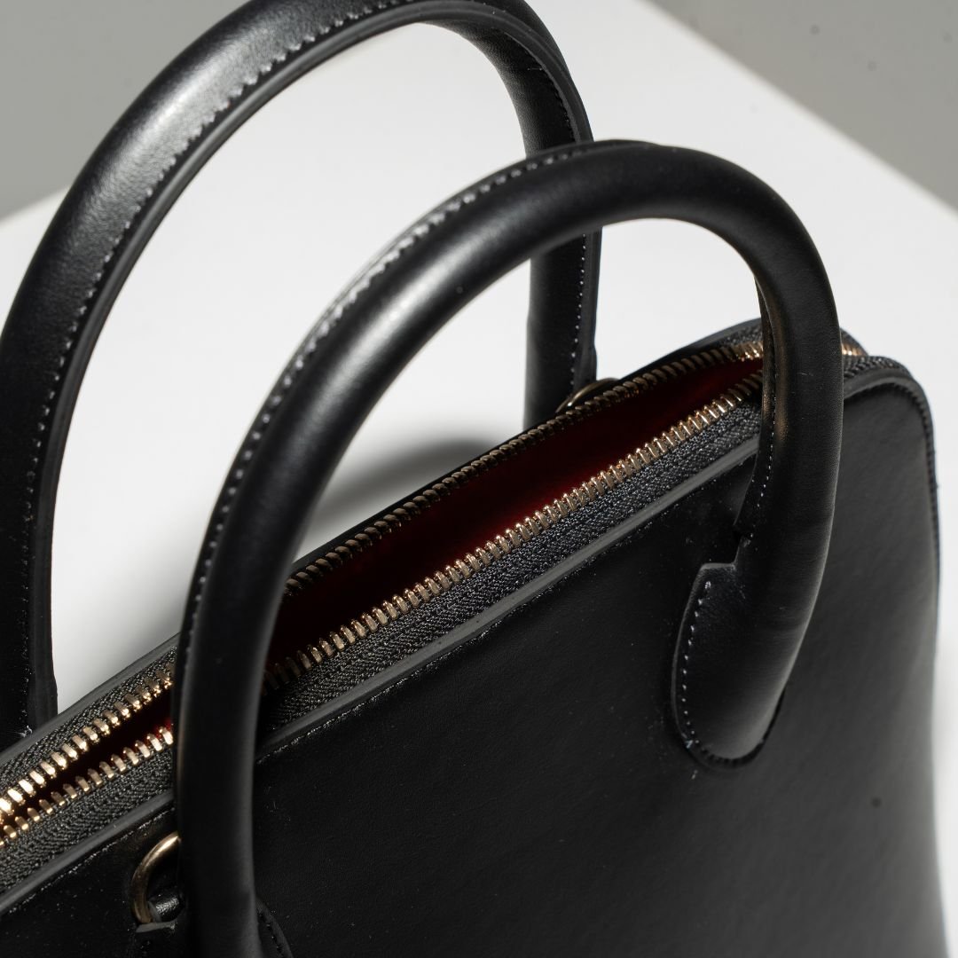  A top-down angle of Ms. Lady Luck in Noir, emphasizing its elegant curves, premium stitching, and spacious zippered opening. The classic black grape leather exterior makes this handbag a wardrobe essential for any occasion.